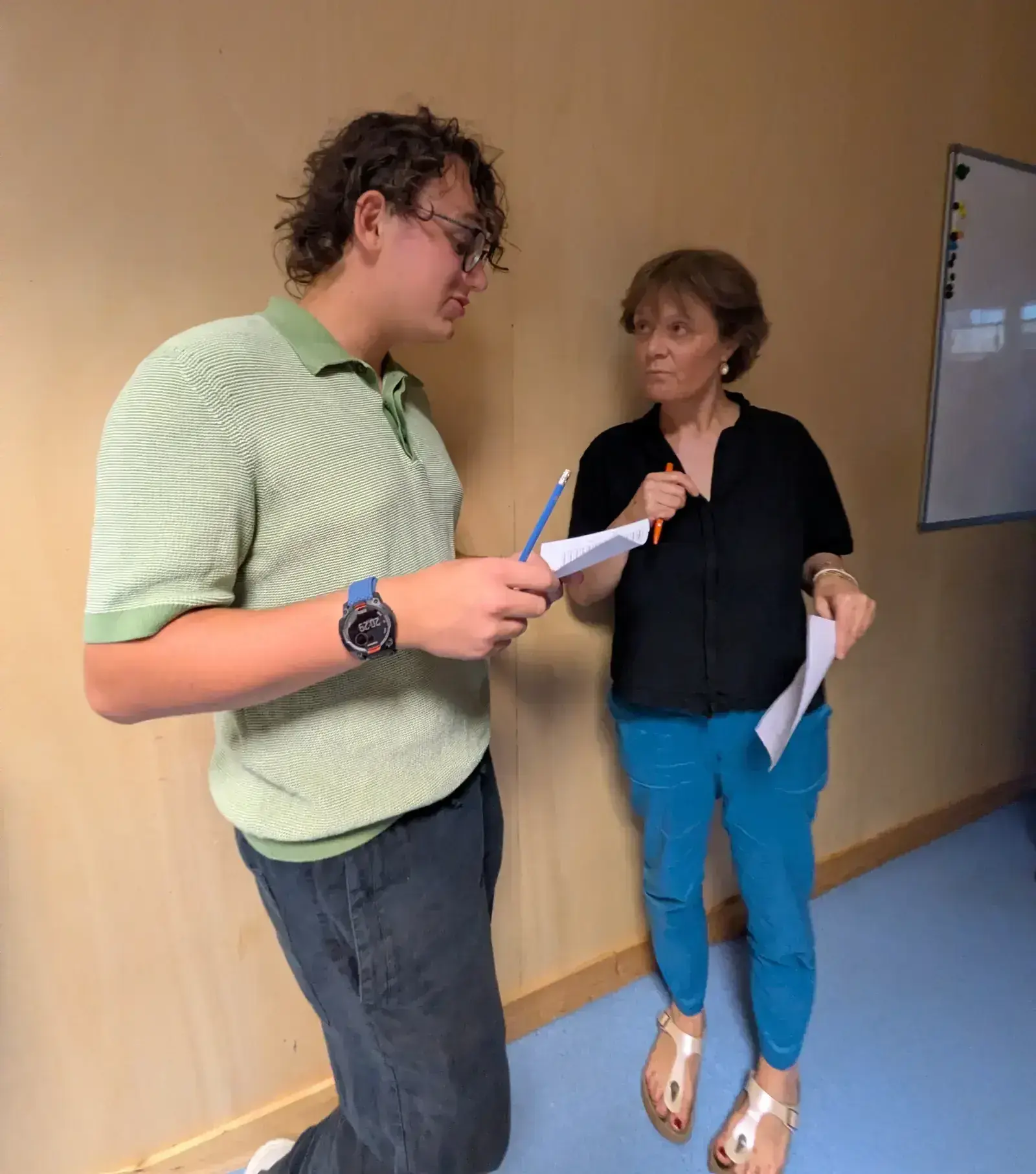 Deux participants échangent, feuille à la main, devant un mur en bois clair