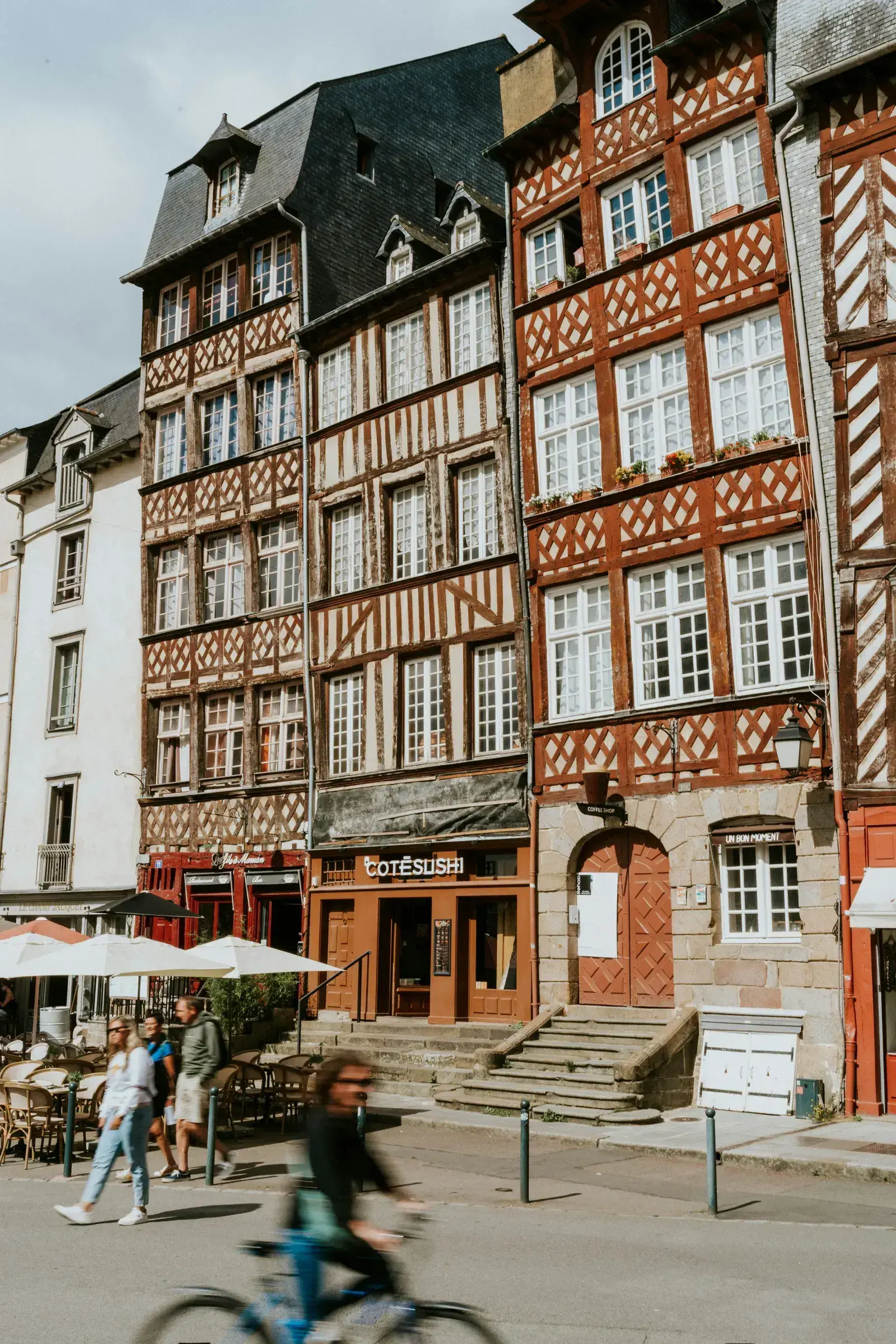 Maisons à pans de bois du centre historique de Rennes, avec des terrasses de café et un cycliste