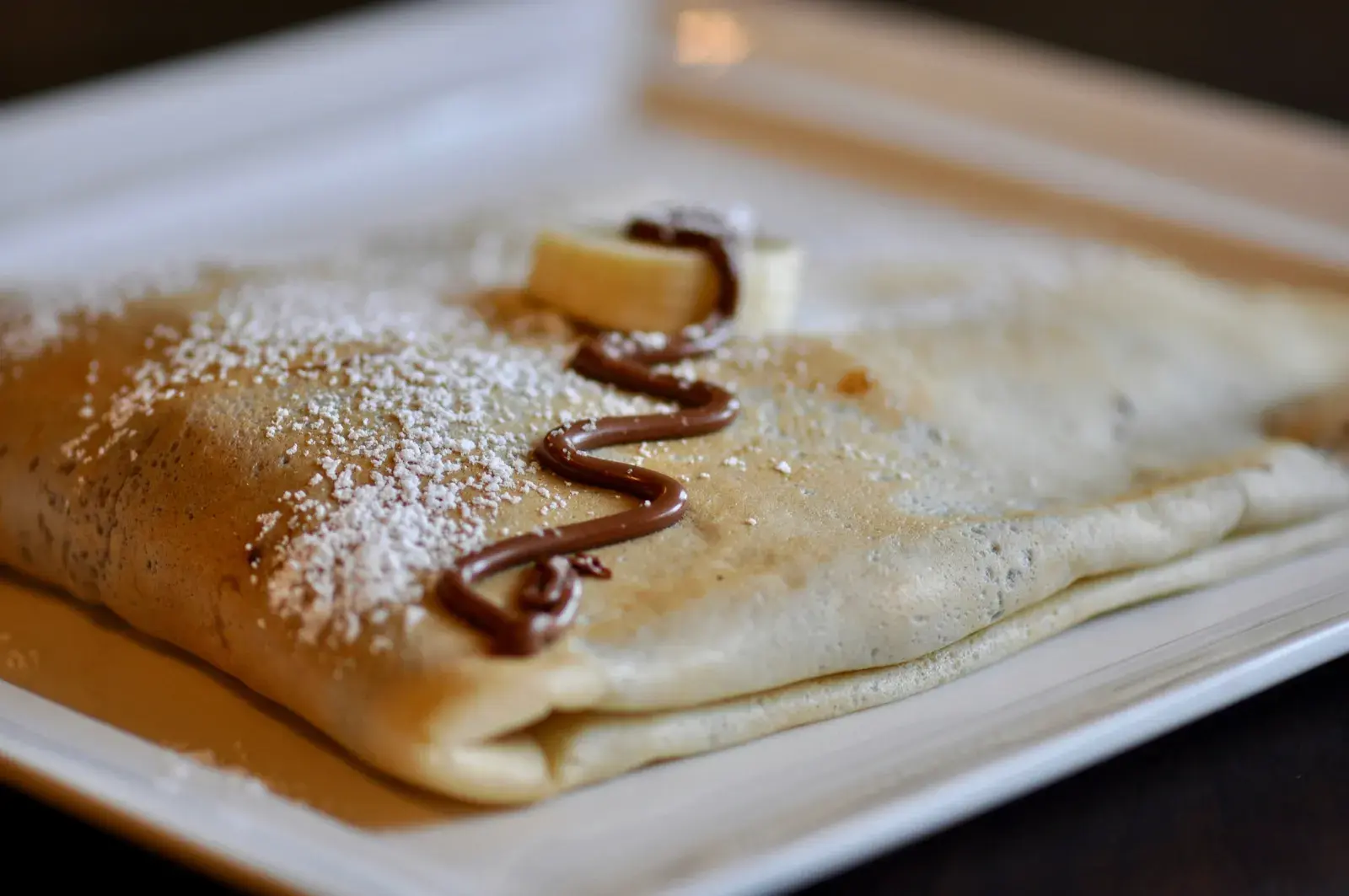 Crêpe sucrée pliée sur une assiette, saupoudrée de sucre glace et nappée de chocolat